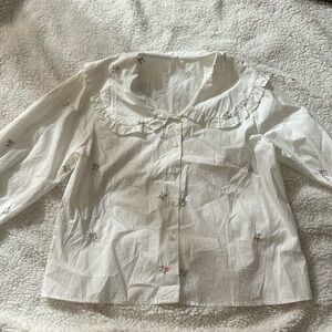Button up shirt. Collar has ruffles around it. Blue and pink embroidery pattern